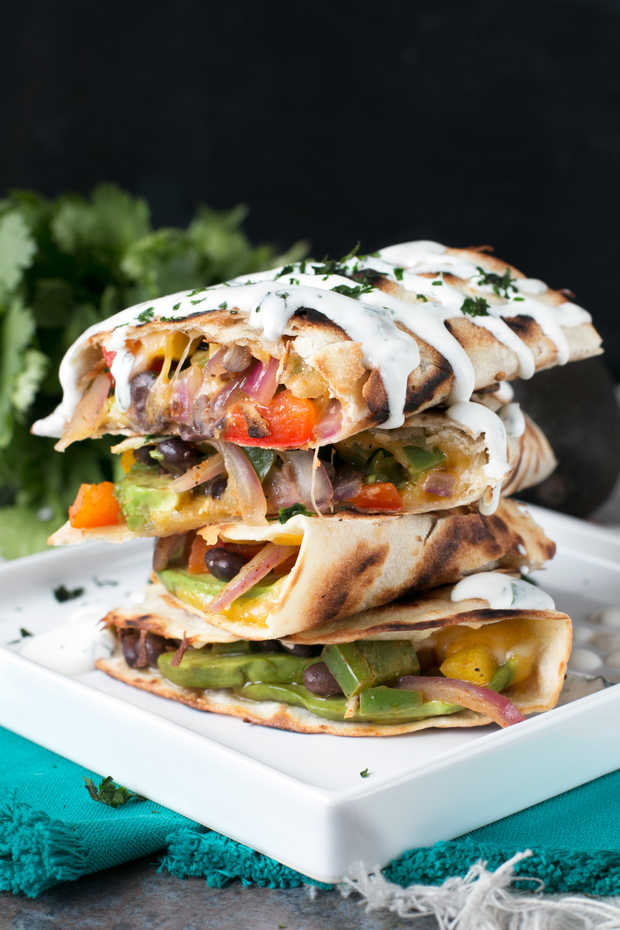 A stack of veggie quesadillas with white sauce on top.