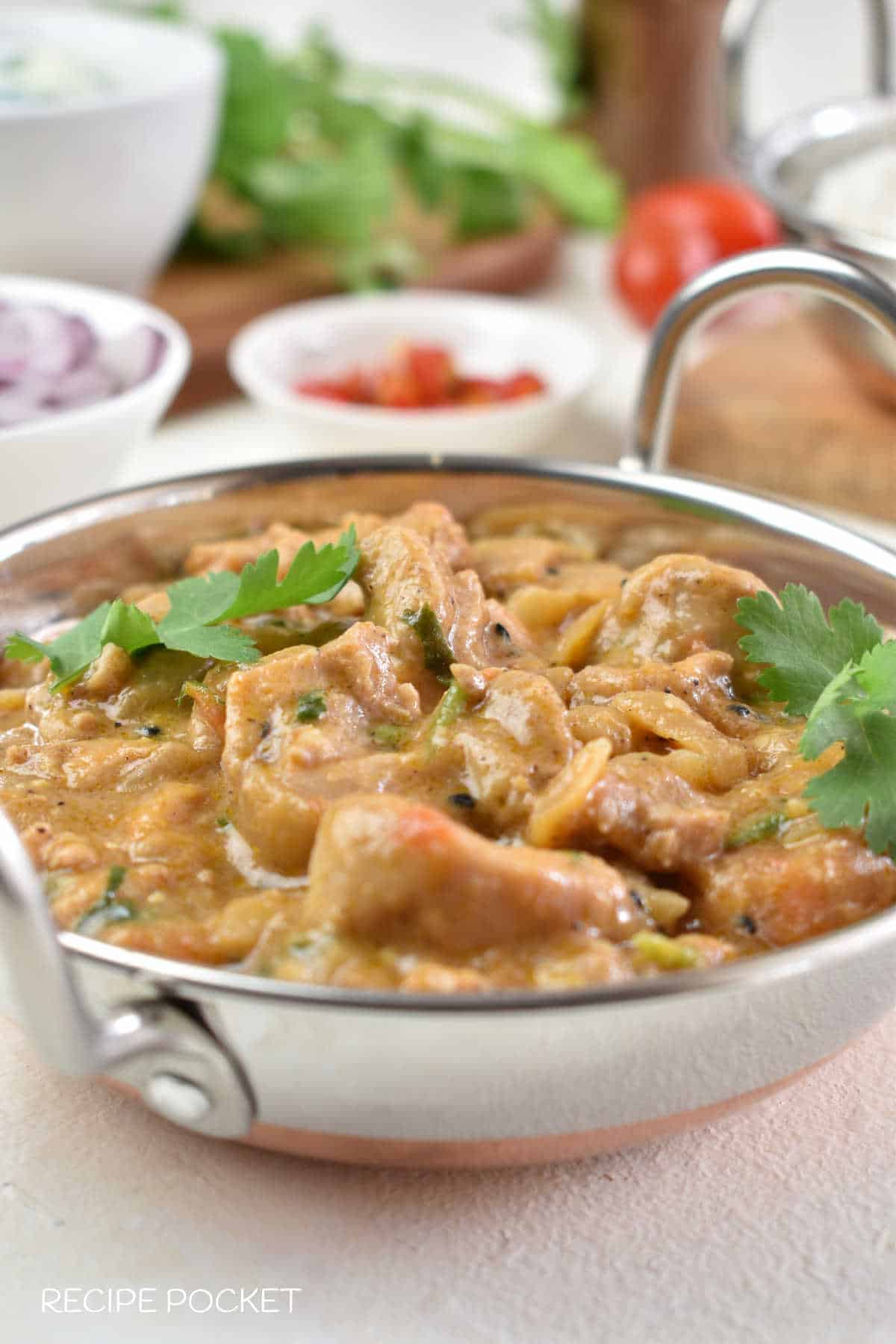 Balti chicken curry on a table with various dishes in the background.