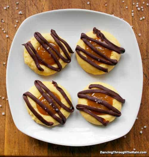 Four salted caramel cookies with chocolate drizzle on a white plate.