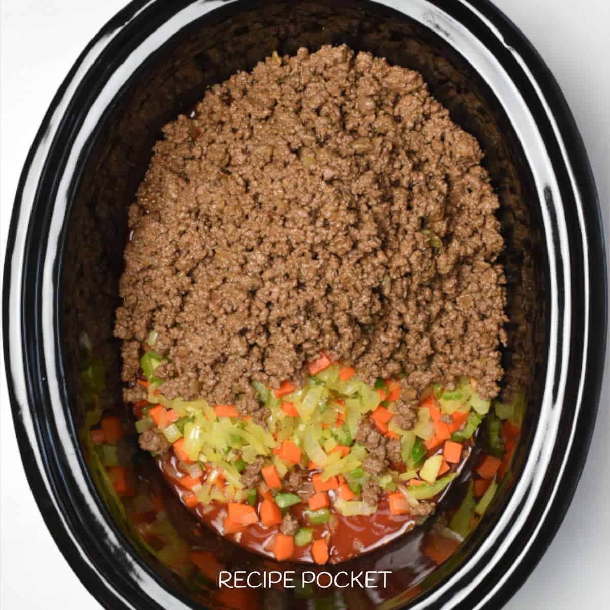 Ground beef in a slow cooker bowl with tomatoes and cooked vegetables.