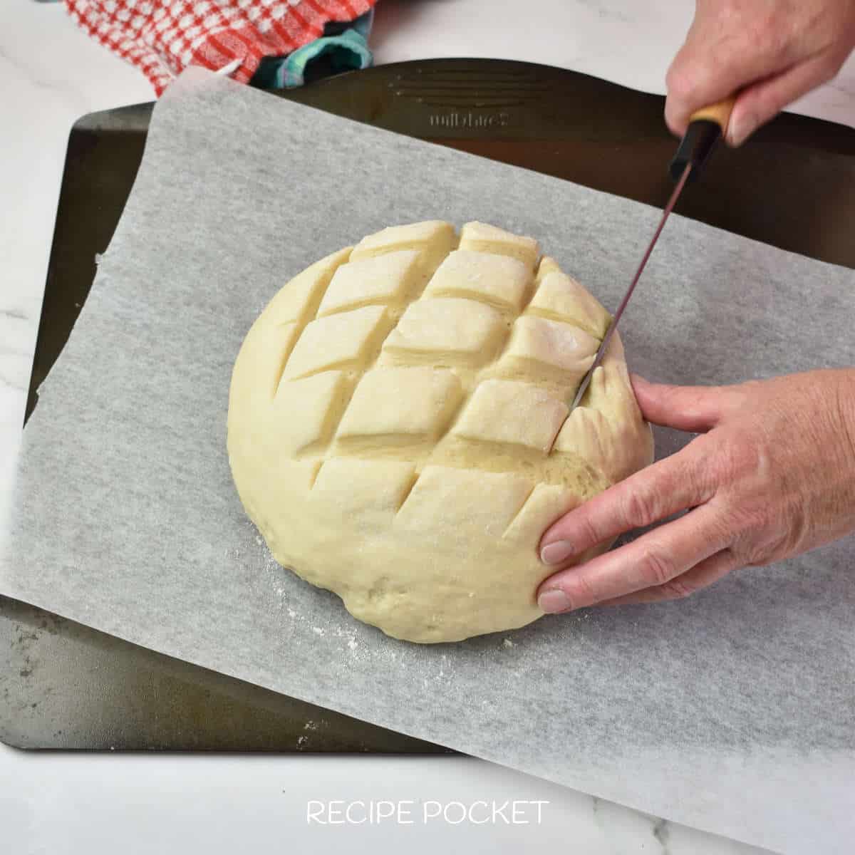 Bread dough being scored with a knife.