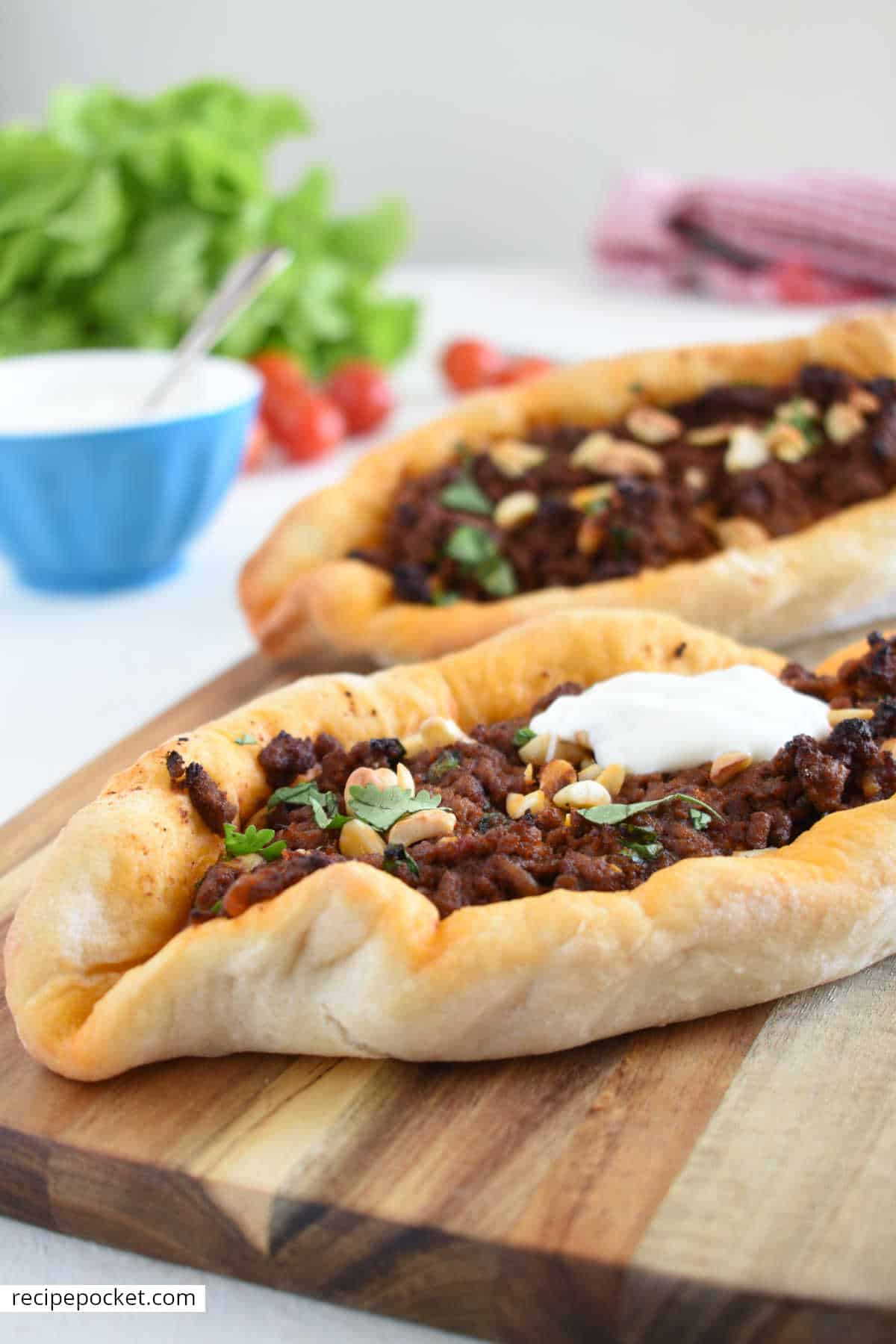 Two Turkish pide pizzas on a wooden board garnished with natural yogurt.