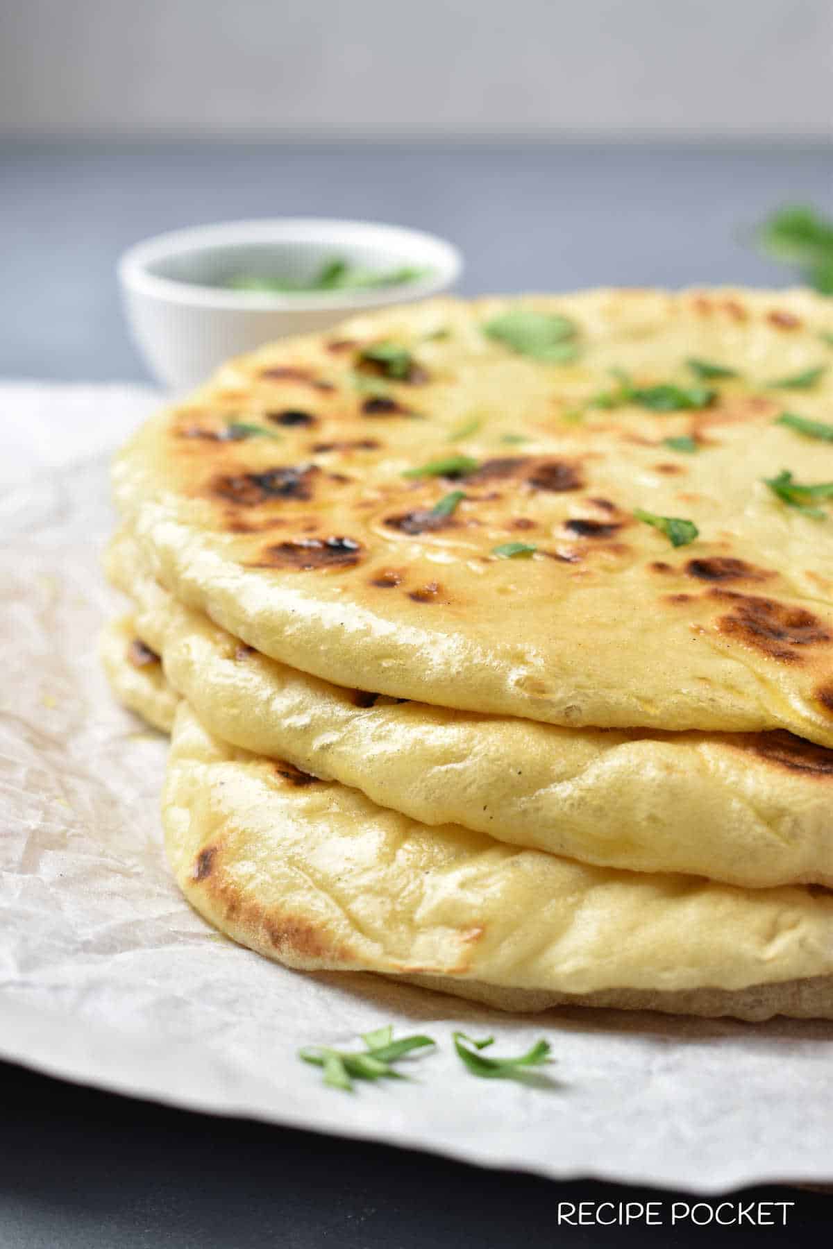 A stack of naan bread on baking paper with a white bowl in the back.
