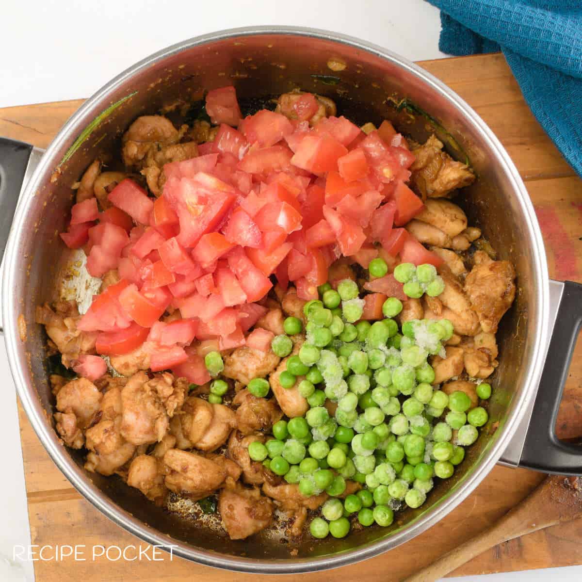 Cooked chicken, tomato and peas in a pot.