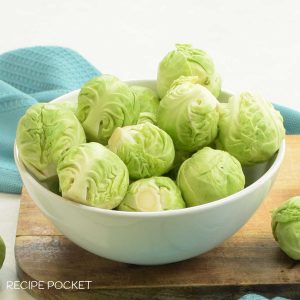 Close up of Brussel sprouts in a white bowl with a green cloth in the background.