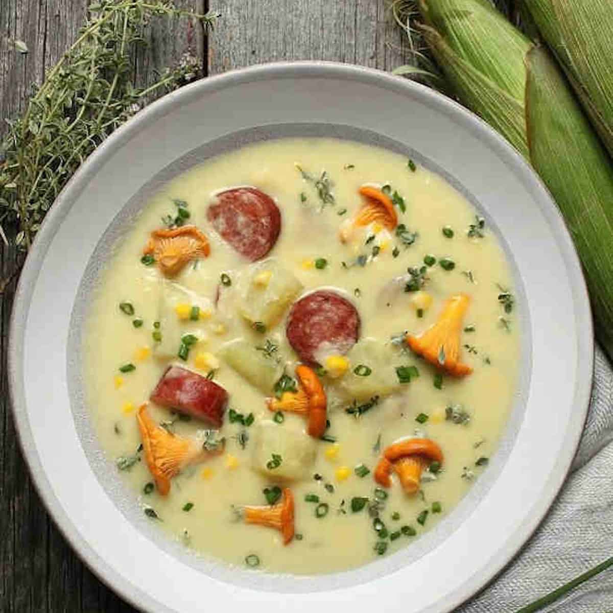 A white soup bowl with sausage and corn chowder.