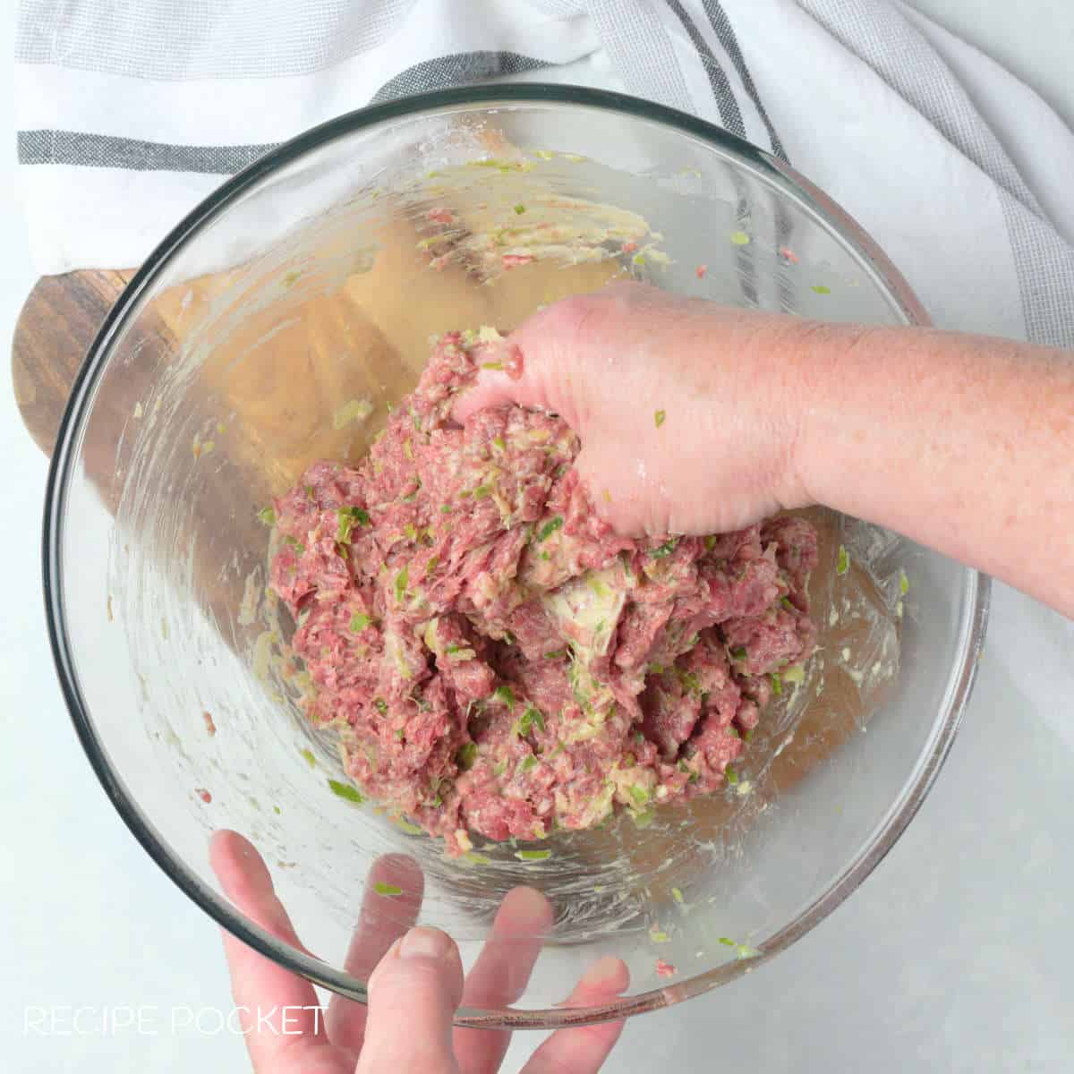 A hand mixing ground beef and other ingedients together.