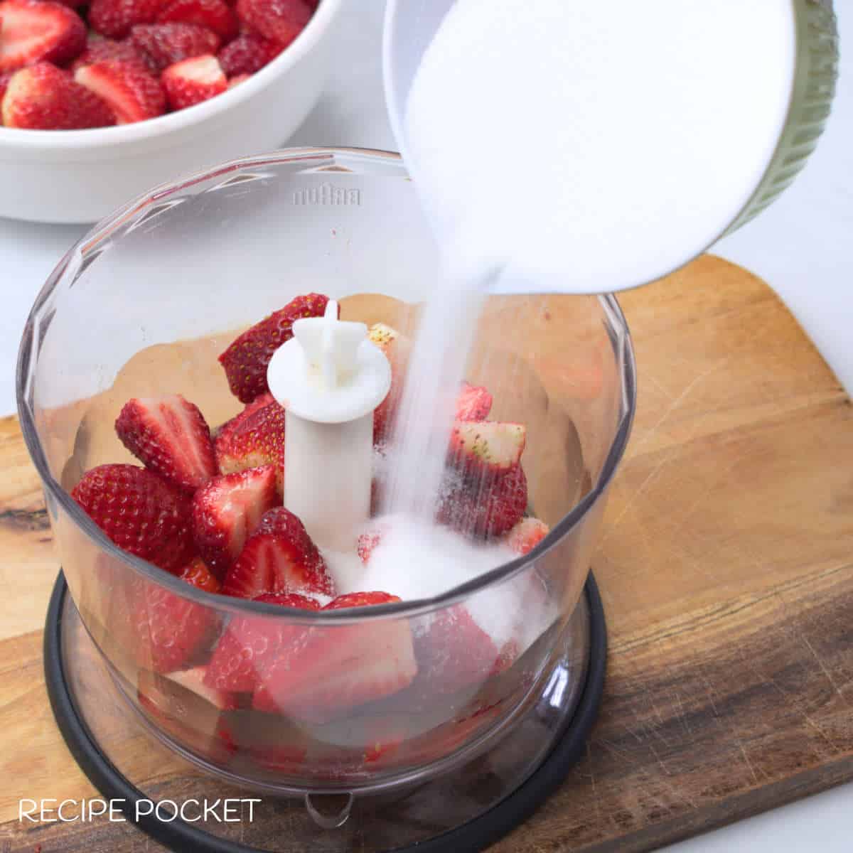Sugar being poured over strawberries in a blender.