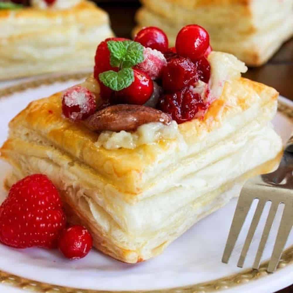Cranberry and brie puff pastry squares on a white plate with a fork.