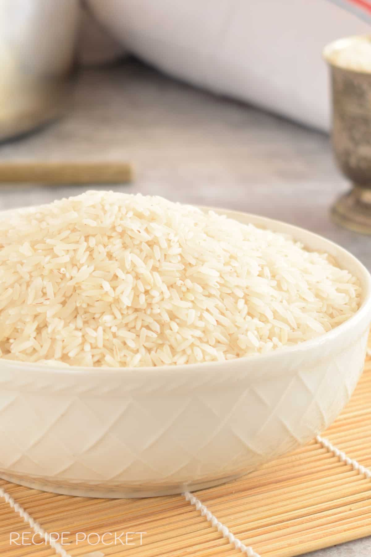 A bowl filled with uncooked basmati rice with a rice bag in the background.