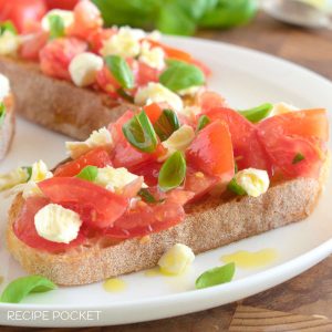 Two pieces of tomato and mozzarella bruschetta on a white plate with fresh basil leaves.