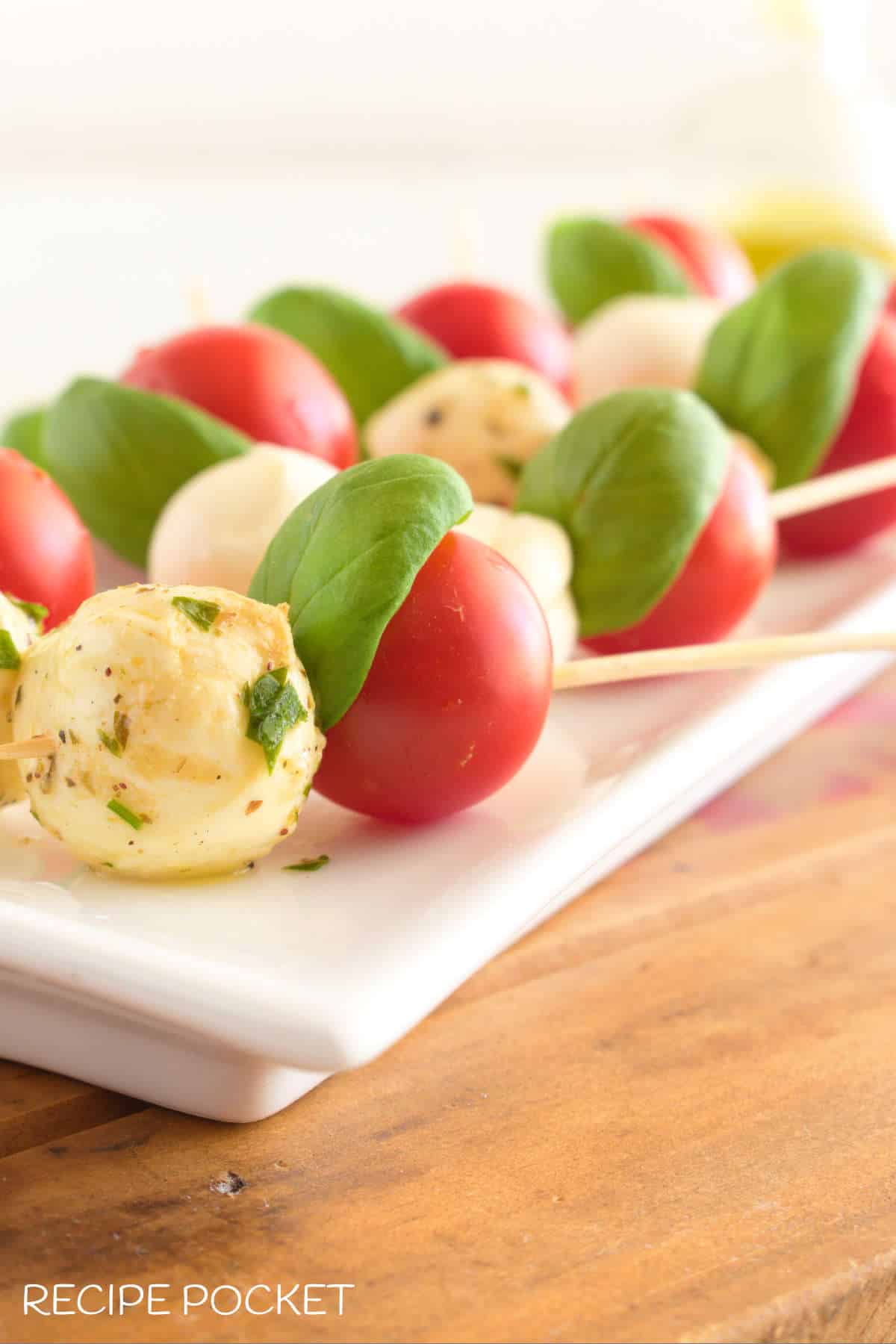 Close up of cherry tomatoes and marinated bocconcini on skewers.