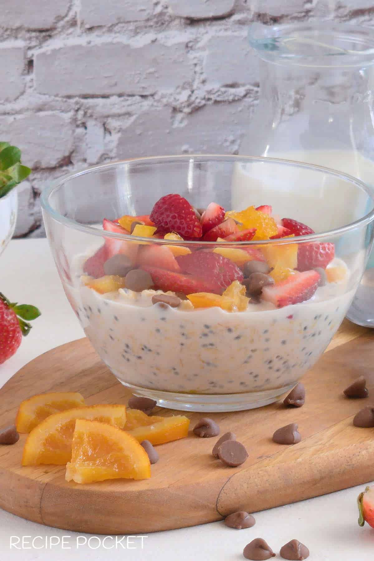 A glass bowl filled with overnight oats with strawberry and chocolate chip topping.