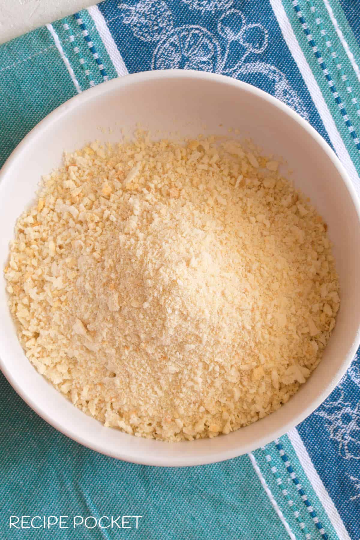 Breadcrumbs in a white dish on a blue green cloth.