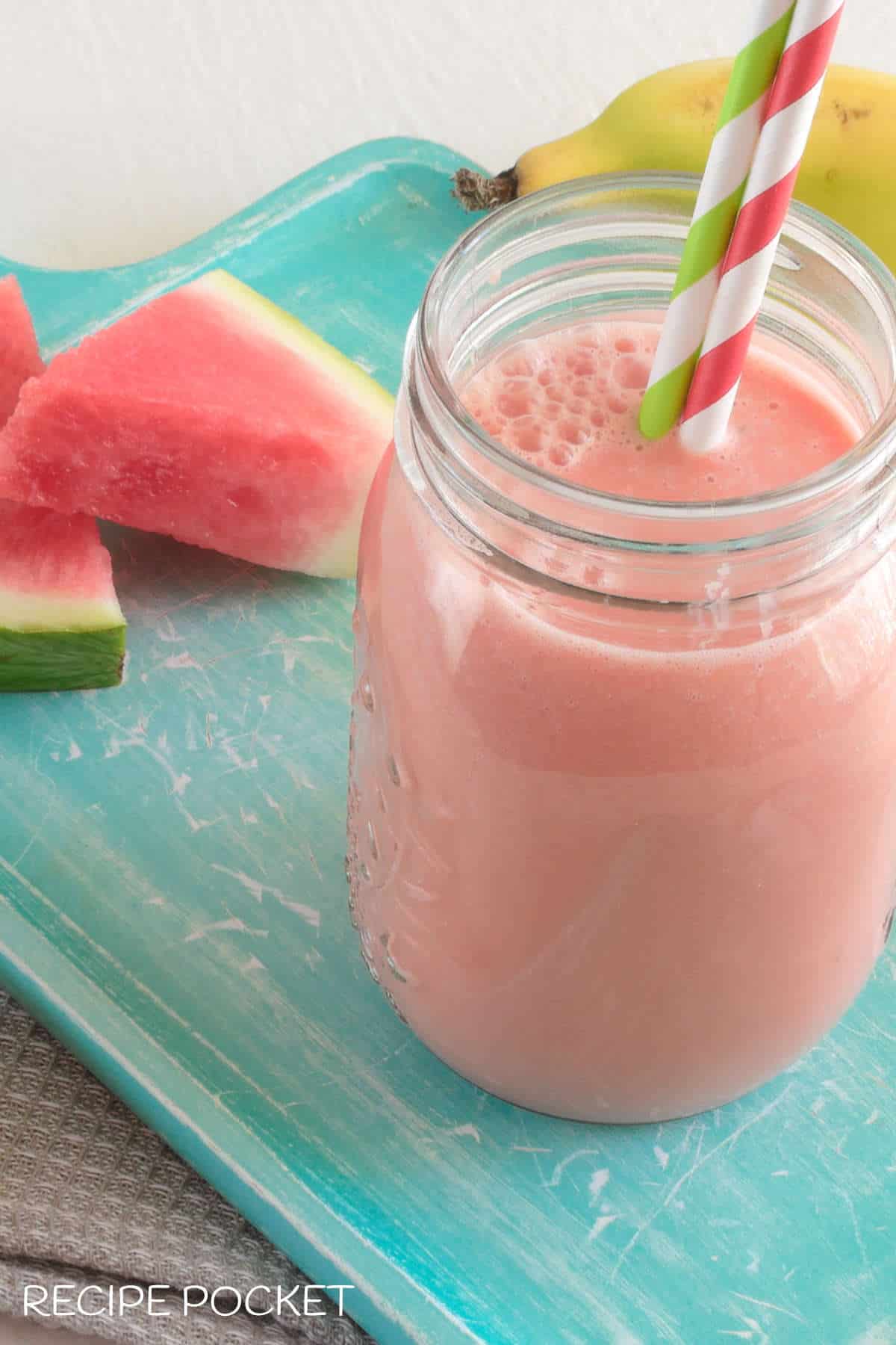 A watermelon smooth in a glass bottle with two drinking straws.