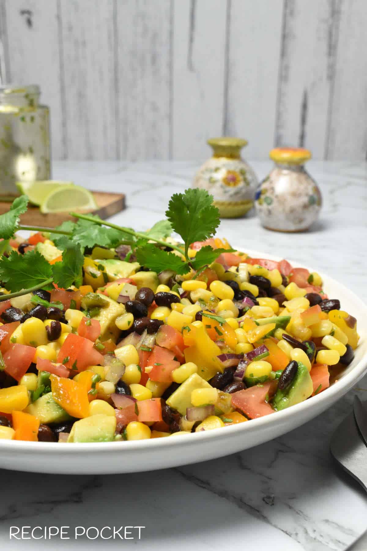 A side view of a plate of black bean corn and avocado salad on a table.