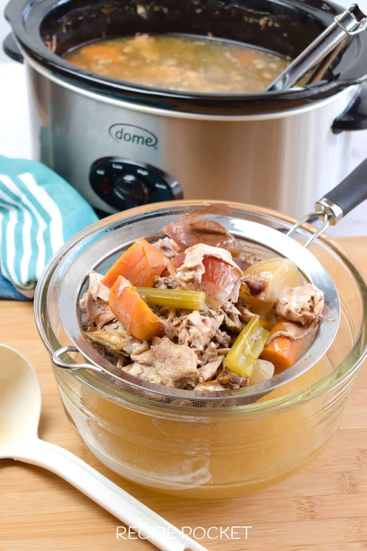 Cooked chicken bones and vegetables in a strainer.