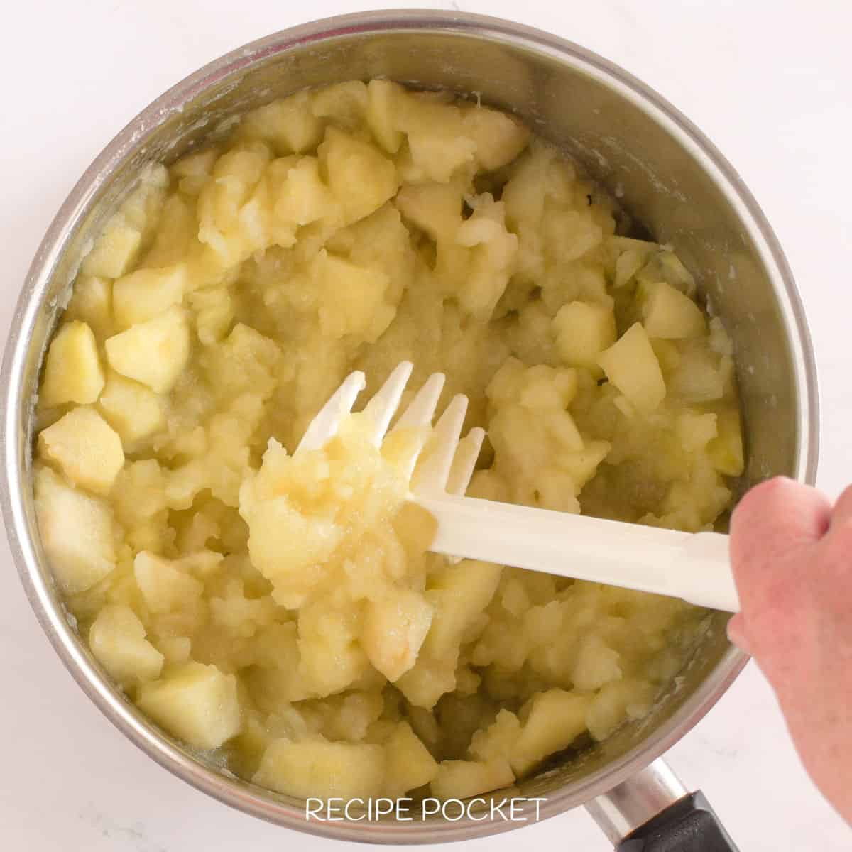Cooked apples being mashed in a saucepan.