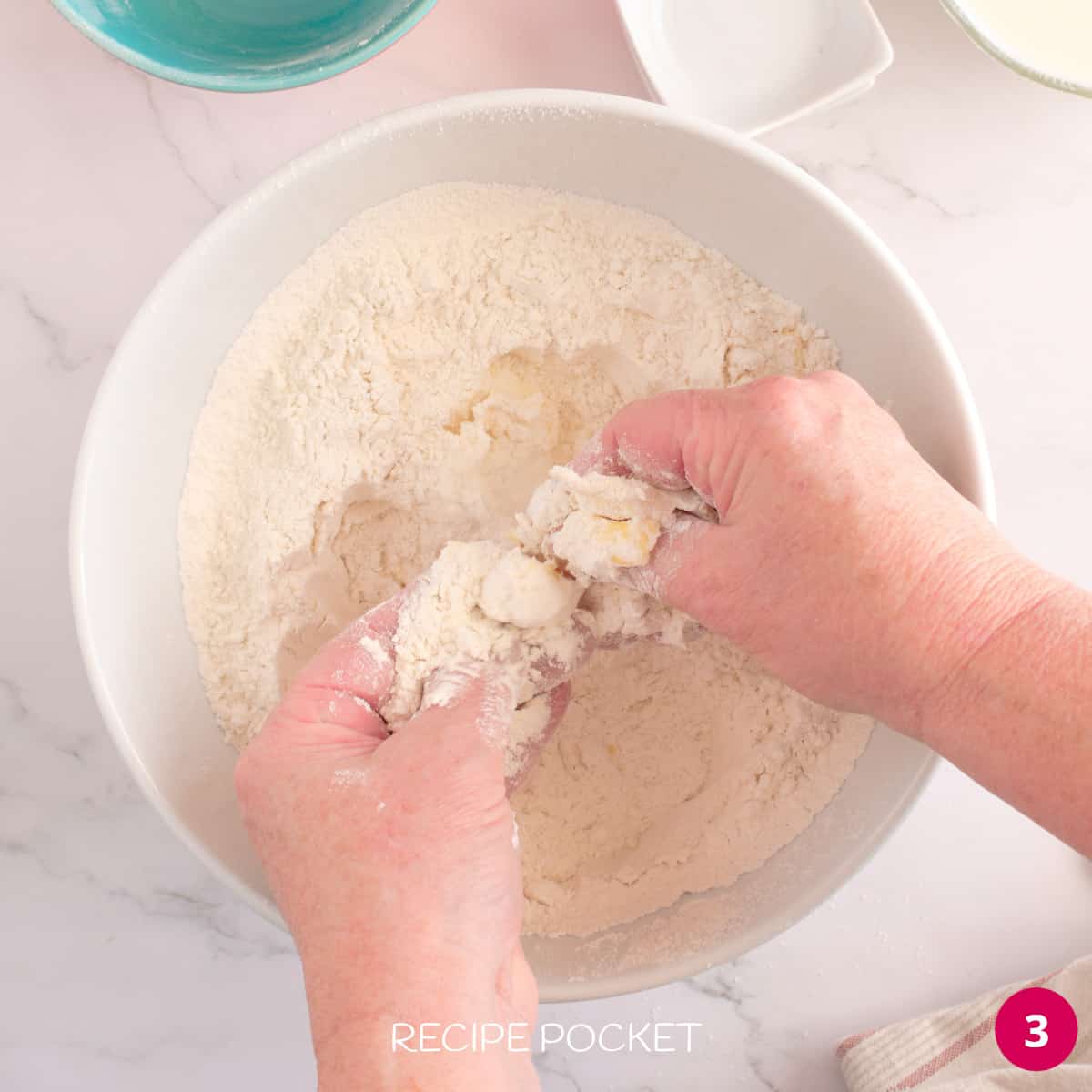 Hands crumbling butter into flour.