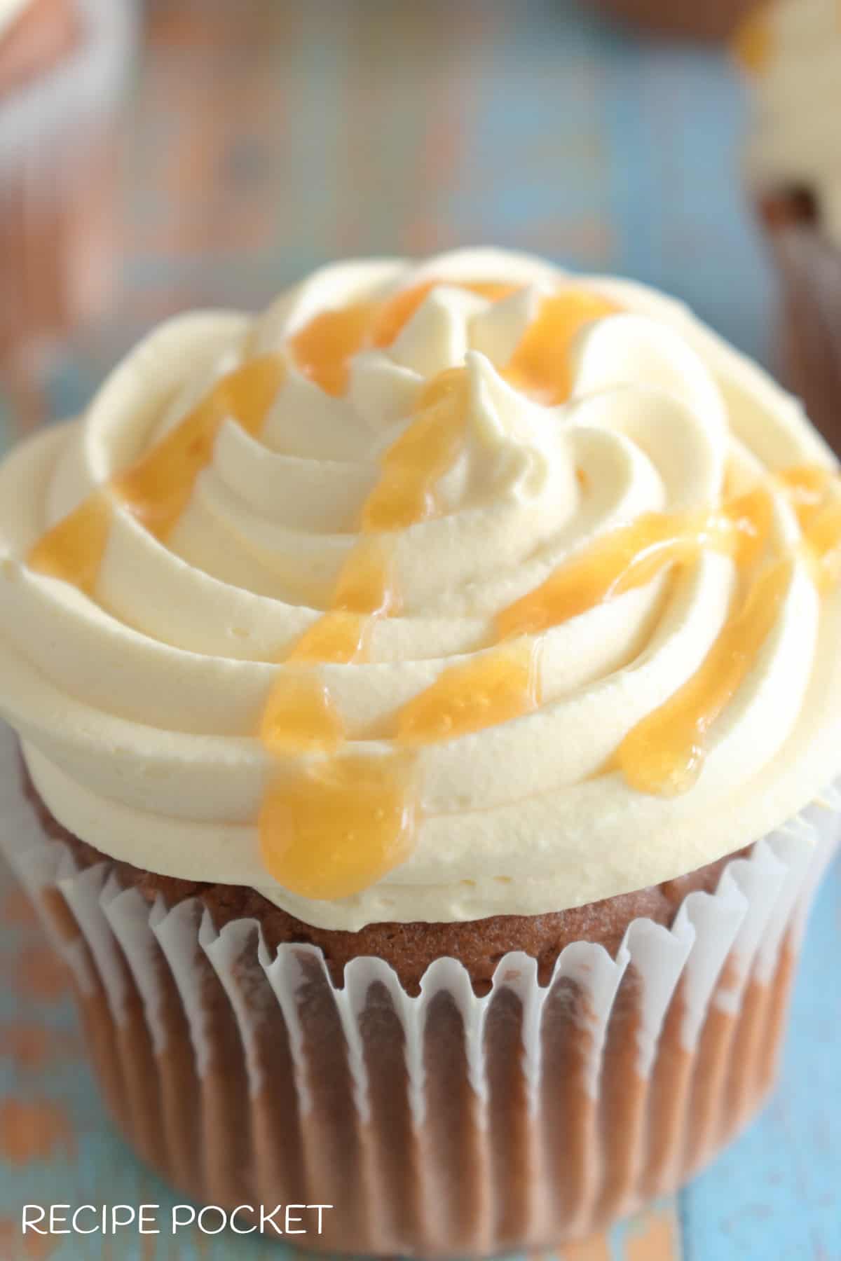 Caramel whipped cream on a cupcake with caramel sauce drizzled over the top.